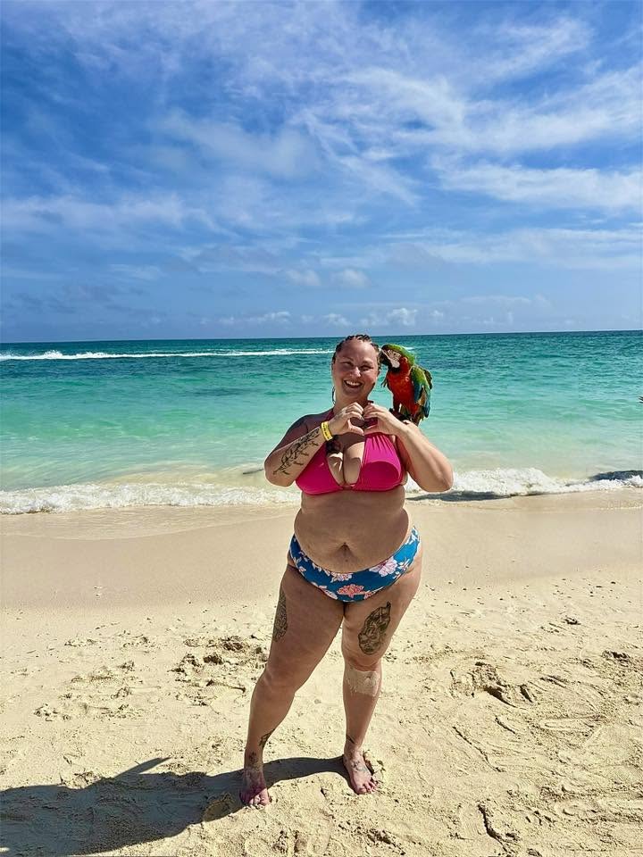 Jess making a heart with her hands beside a parrot on the beach