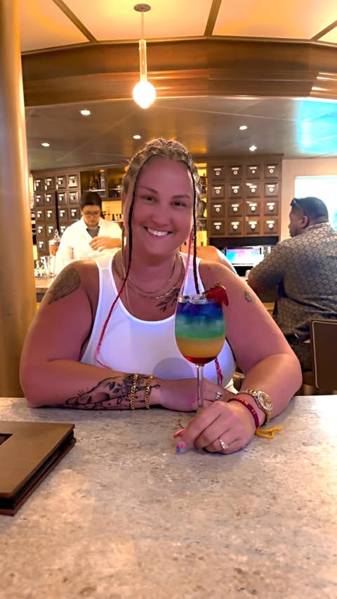 Jess smiling at a bar with a colorful rainbow cocktail